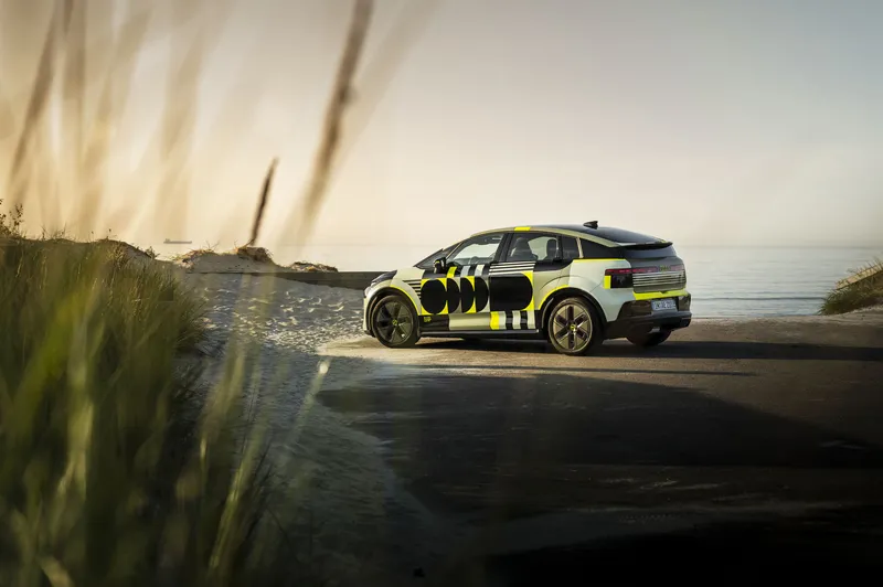 Gul och svart Audi e-tron elsuv parkerad på smal väg vid stranden med höga gräs och hav i bakgrunden.