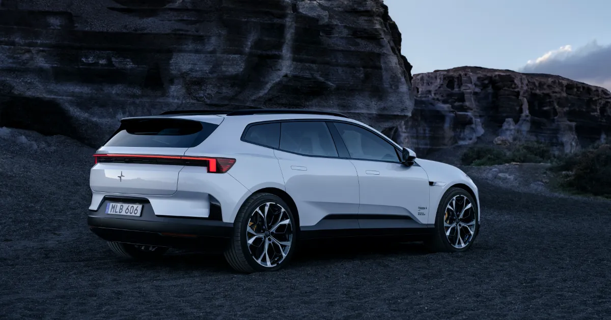 Silvervit Polestar 4 SUV snett bakifrån med upprätt baklucka framför en klippvägg i skymning