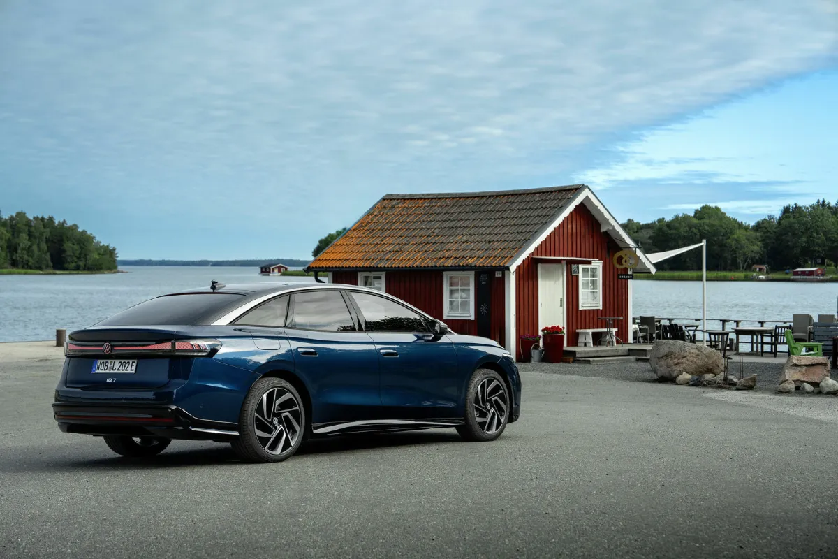 Blå Volkswagen ID.7 Pro S parkerad vid en röd sjöbod vid vattnet