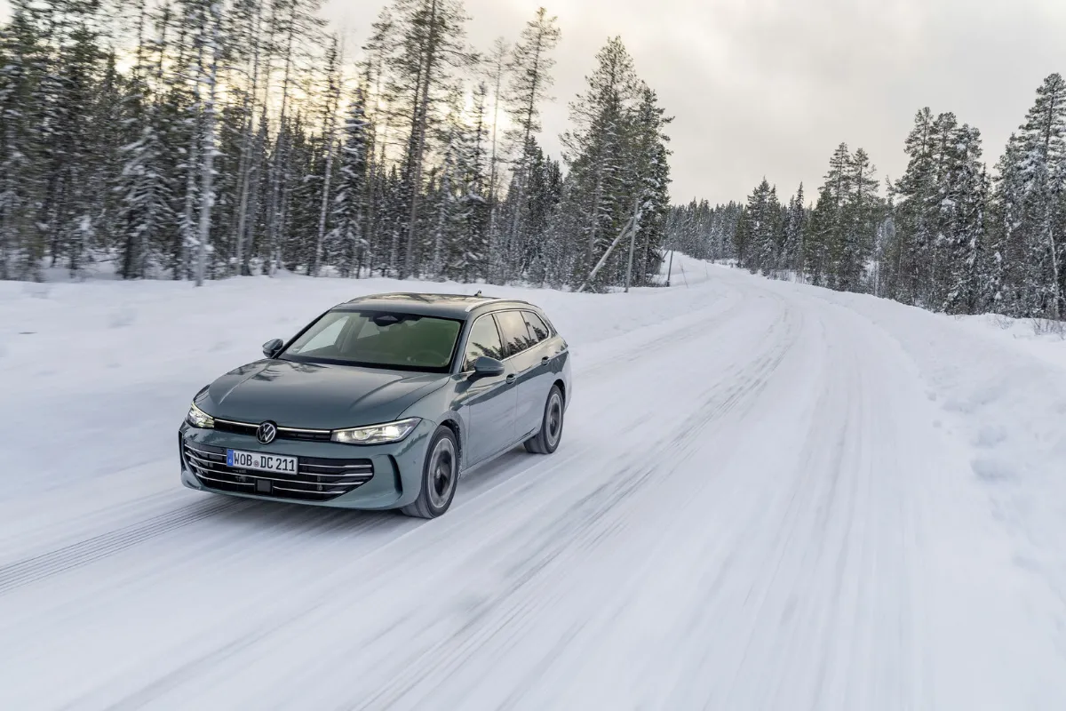 Grå Volkswagen Passat kör på en snötäckt väg genom granskog